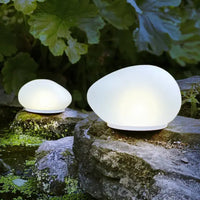Two spherical outdoor lights on rocks with greenery in the background